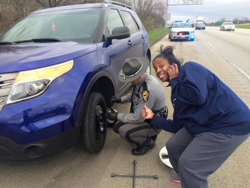 Black woman getting help changing tire from policeman